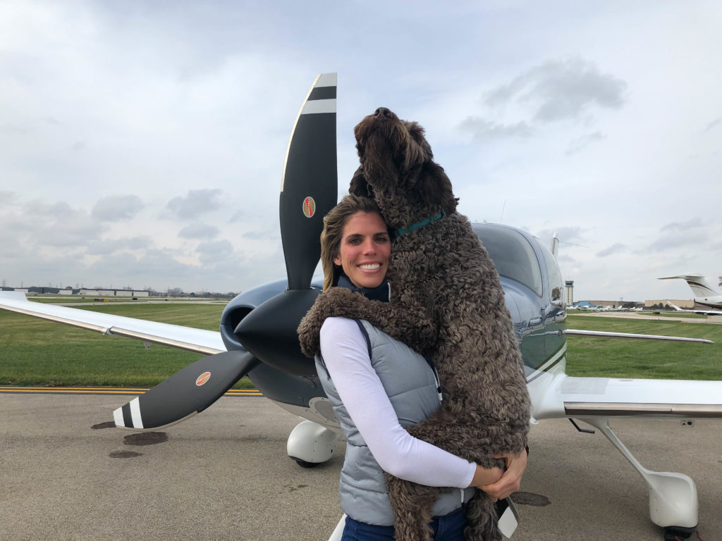 Pilot Amy Voss holding her dog Murph, standing in front of an airplane.