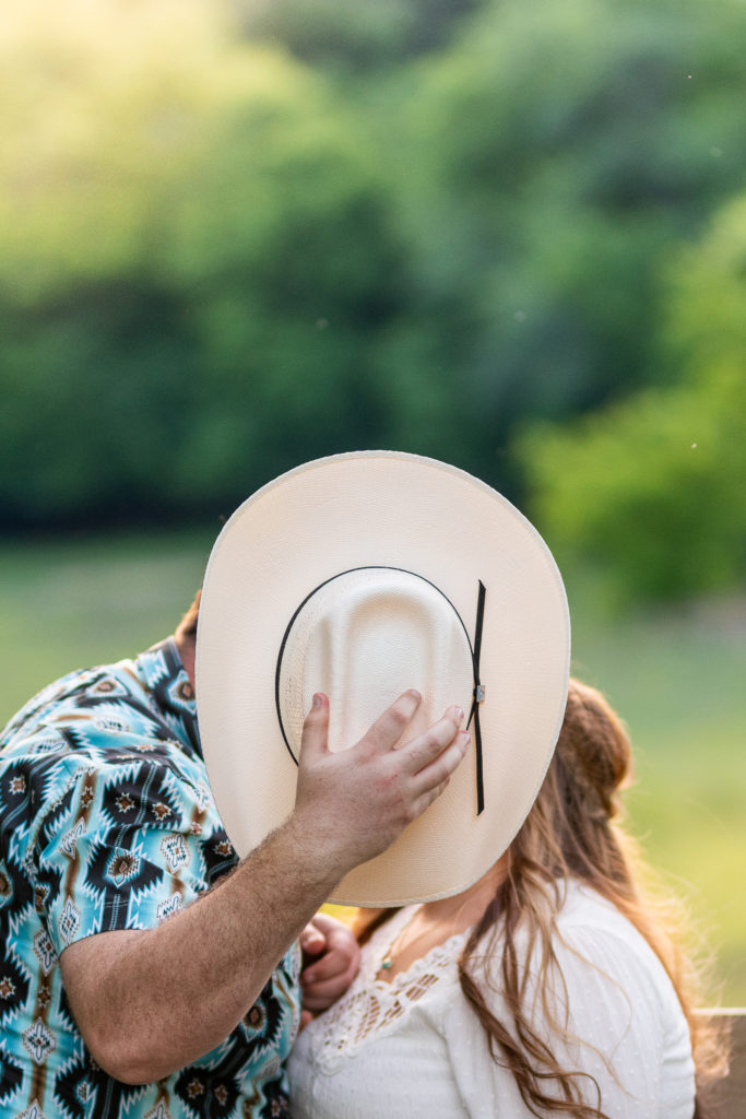 A couple hiding behind a cowboy hat, pretending to kiss for their engagement photos.