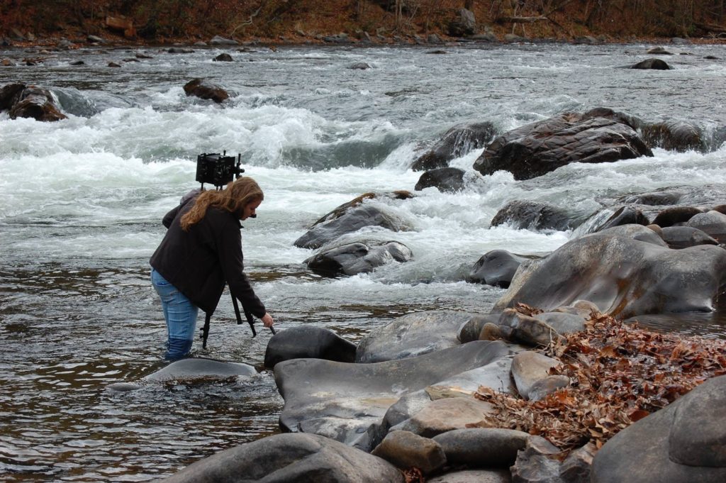 Haley Hensley Photography getting ready to take a picture, standing in the water of a river.