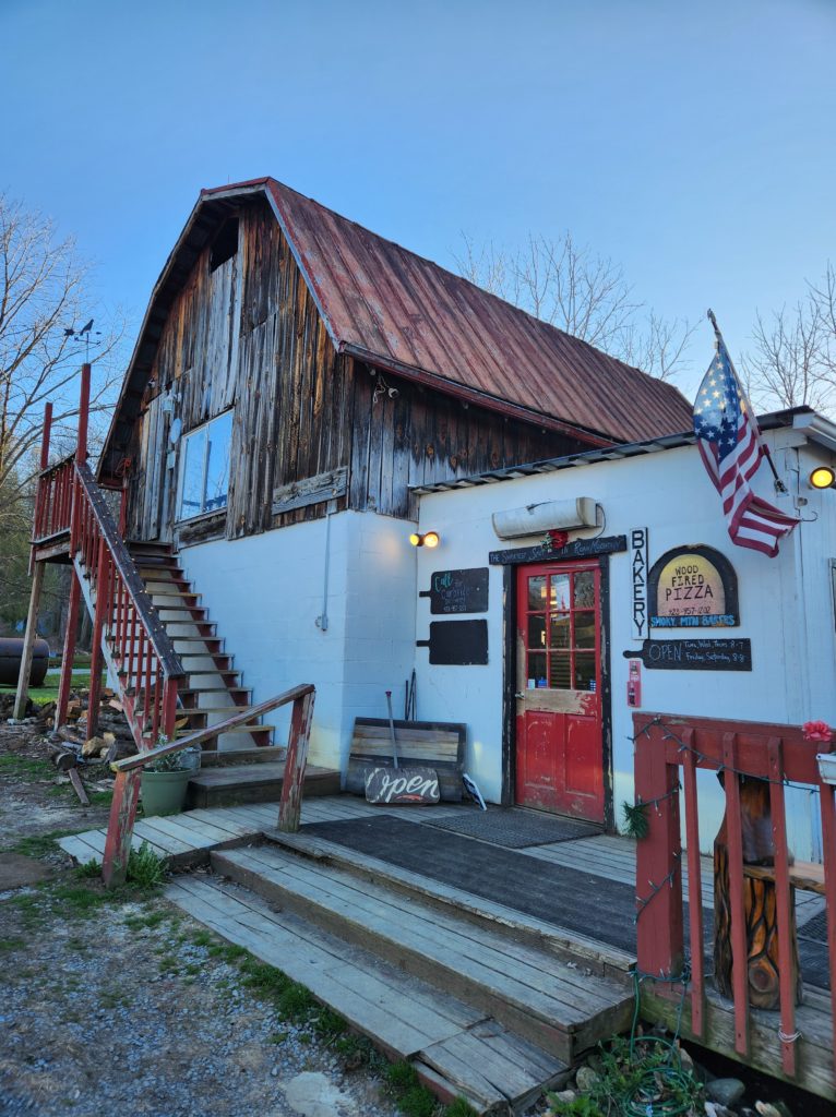 A building that has a dark metal roof, stairs on the front, and a red door leading inside. 