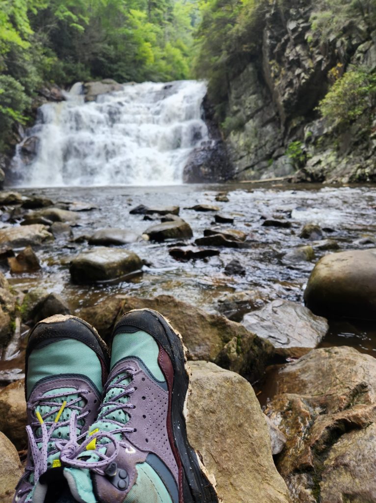 Colorful hiking boots propped up on a rock, with a waterfall in the background. 