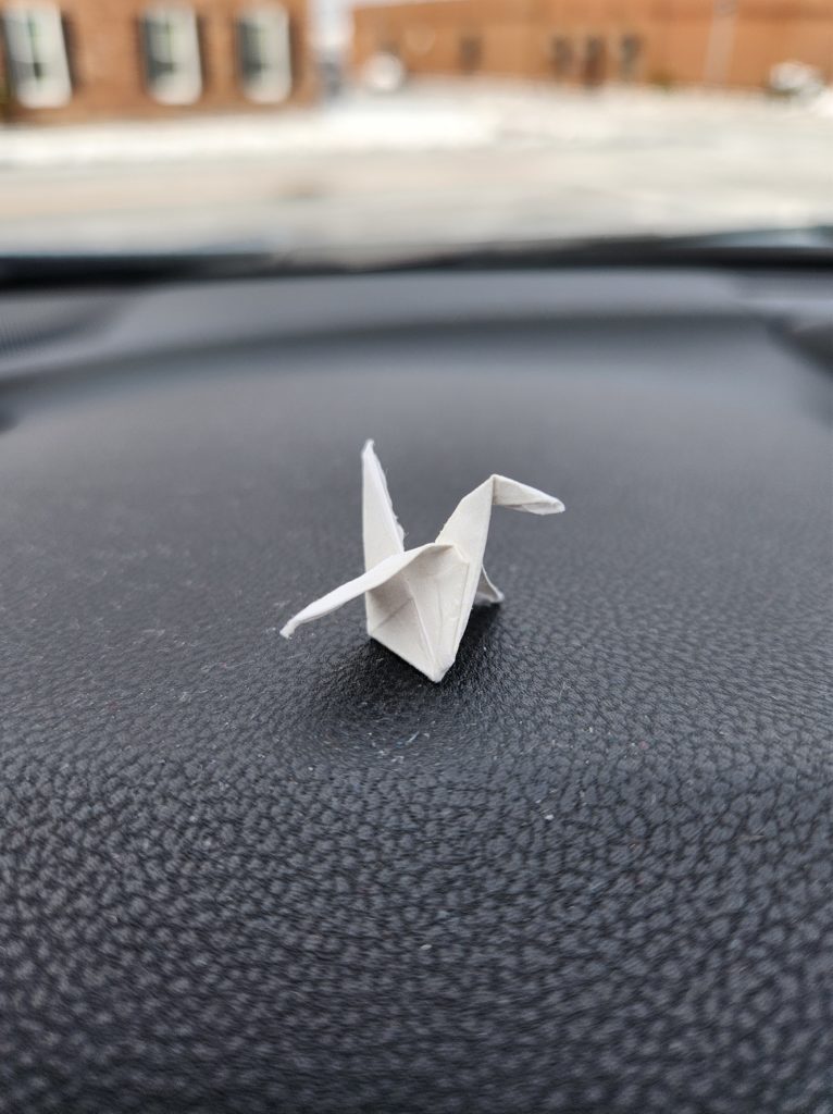 A small origami crane sitting on a cars dash. This is one of the small ways that I give myself permission to fail.