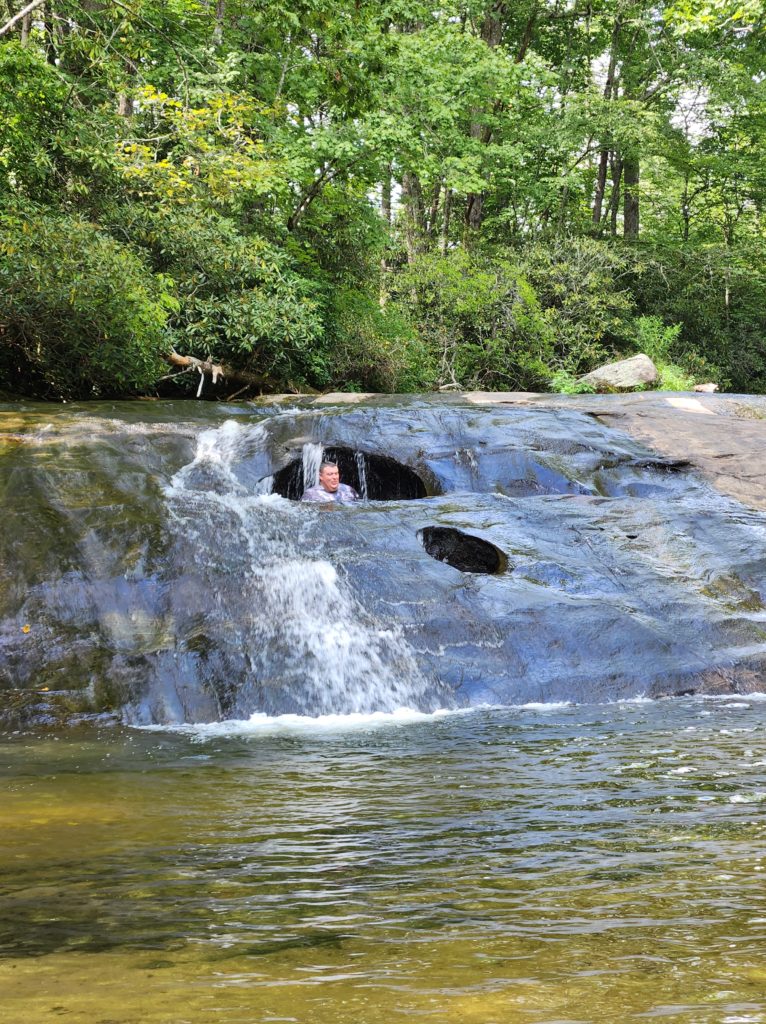 Cashier's Sliding Rock in NC. A man slid down into one of the large, deep holes that the water created. Just his head is sticking out above the water and rocks.