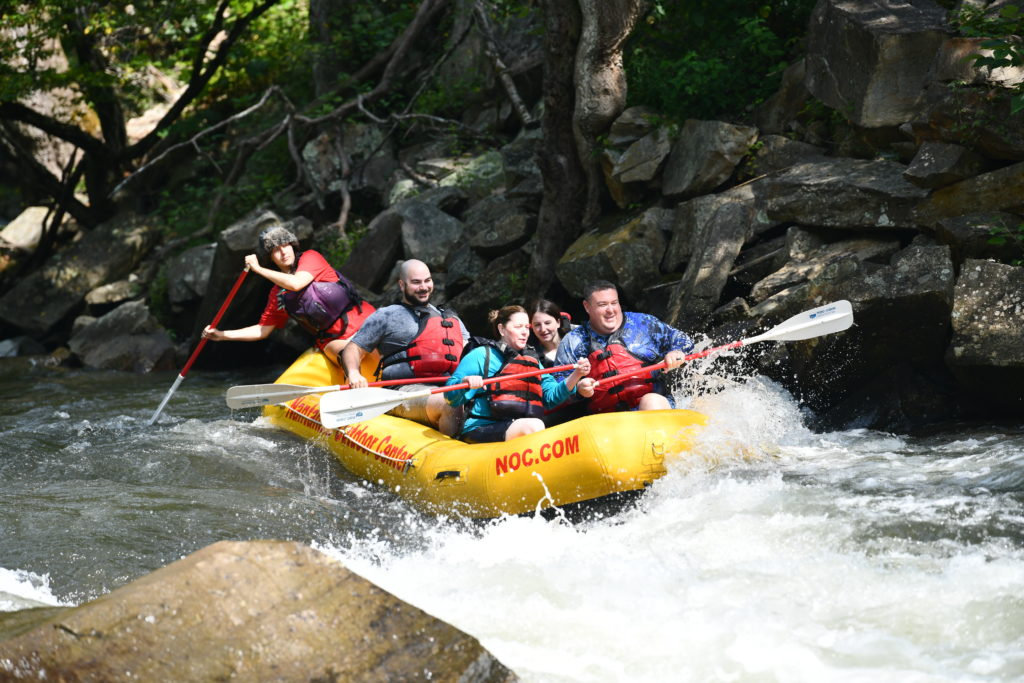 Five people in a white water raft, getting ready to go over the rapids. 