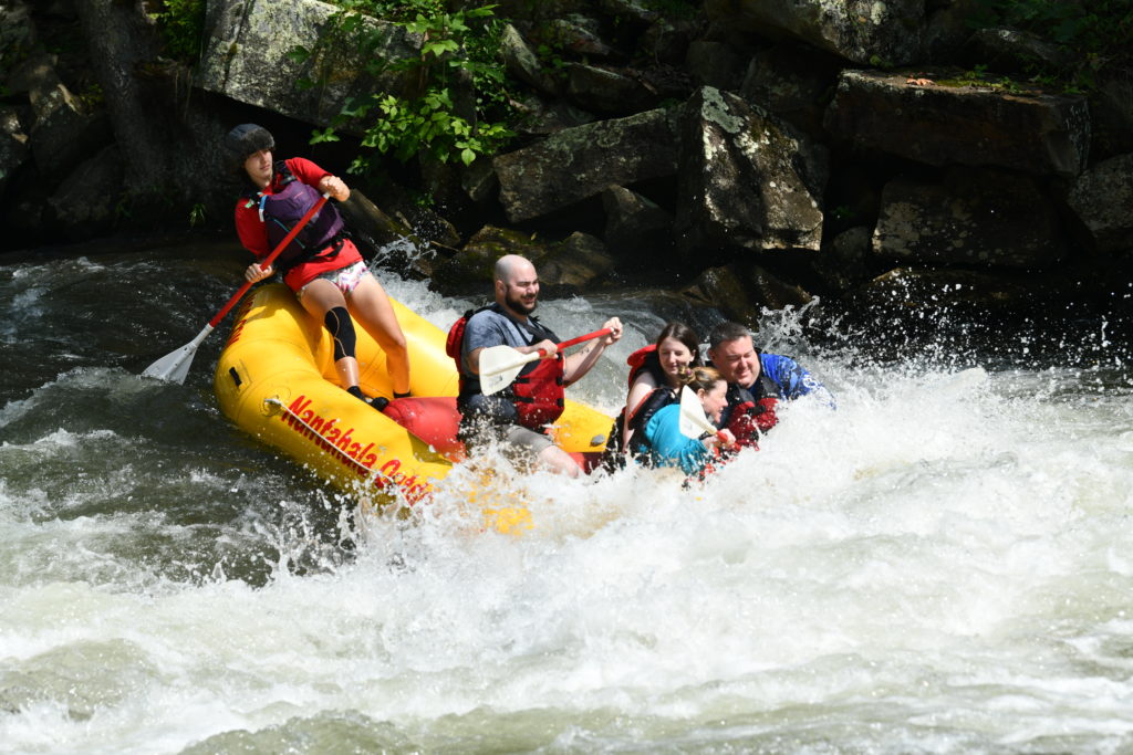 Five people in a raft, white water rafting through the rapids.
